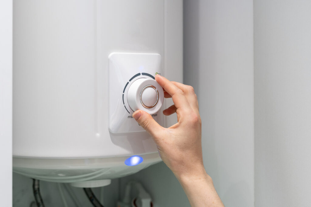 Hand adjusting temperature on boiler hanging on wall, using control knob.