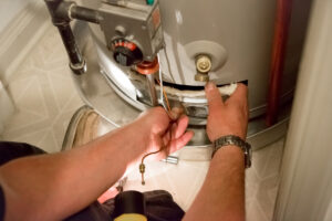 A person's hands are working on a water heater in a closet.