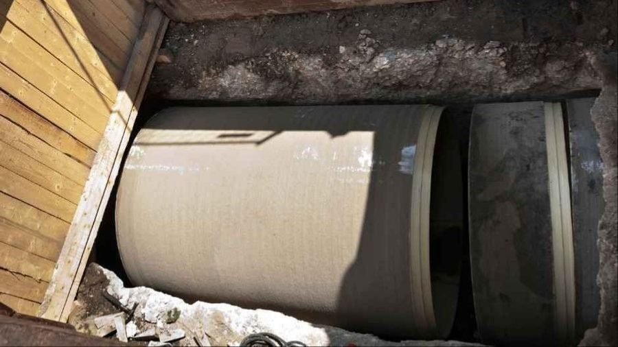 Large concrete pipe laid in a construction trench, surrounded by dirt and wooden boards.